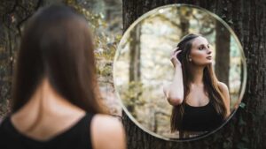 Woman looking in mirror in the forest to show that excessive vanity is a toxic Libra trait.
